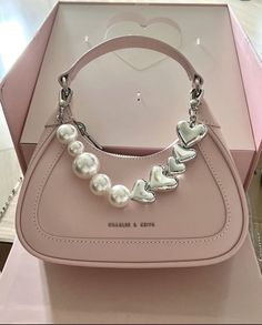 a pink handbag with pearls and hearts on the front is in a box for display