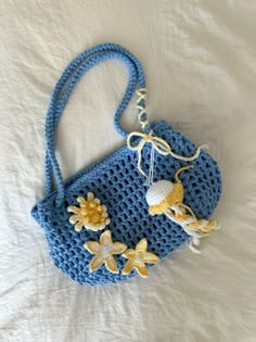 a crocheted blue purse sitting on top of a white bed next to a stuffed animal