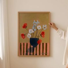 a woman standing next to a painting on the wall with red, white and blue flowers in it