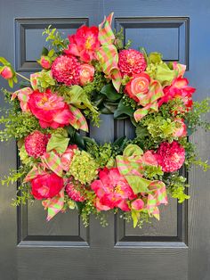 a wreath with pink flowers and green leaves on the front door to a house or business