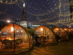 several glass domes with tables and chairs in front of a cityscape at night