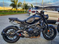 a black motorcycle parked in a parking lot next to other cars and suv's