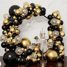 a black and gold balloon arch with lots of balloons in it on a wooden table