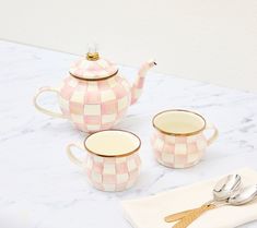 pink and white checkered ceramic tea set with matching spoons on marble countertop