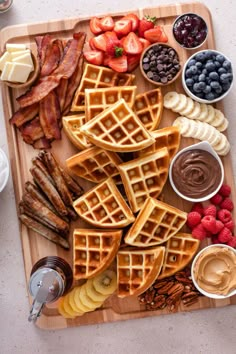 a wooden tray topped with waffles covered in fruit and other foods next to chocolate