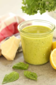 a glass jar filled with green liquid next to sliced lemons and parsley