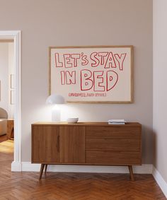 a poster on the wall above a sideboard in a room with hardwood floors and white walls