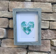 a heart made out of sea glass sitting in front of a stone wall with a frame