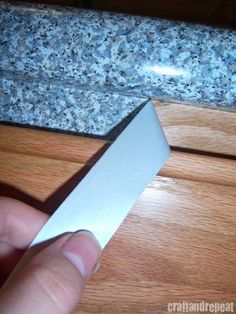 a person holding a knife in their hand on a wooden surface next to a granite counter top