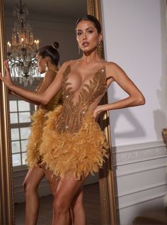 a woman standing in front of a mirror wearing a brown dress with feathers on it