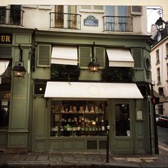 a store front with green shutters and white awnings on the side of it