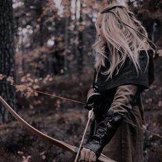 a woman with long blonde hair is holding a bow and arrow in the middle of a forest