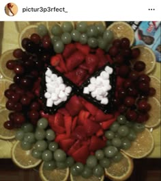 a plate with grapes, oranges and other fruit arranged in the shape of a spider man