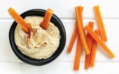 carrot sticks and dip in a black bowl on a white surface with some cut up carrots