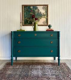 a blue dresser in a room with a painting on the wall and rug underneath it