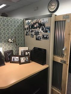 an office cubicle with pictures on the wall and a clock mounted to the wall