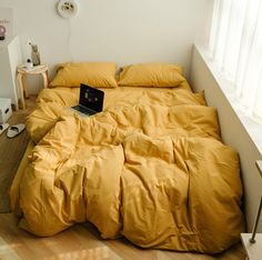 an open laptop computer sitting on top of a yellow comforter in a bed room