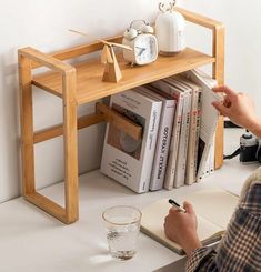 a person sitting at a desk writing in front of a book shelf with books and an alarm clock