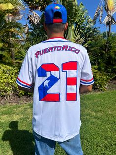 Tainowears Puerto Rico Baseball Jersey. This premium white jersey features bold "PR" embroidery, the iconic Coqui and El Morro in translucent artwork, and vibrant Puerto Rican flag colors on the sleeve. With "WEPA!" embroidered to honor the island’s energy, "Puerto Rico" on the back in PR colors, and the legendary #21 with an intricate flag design, this jersey embodies Puerto Rican pride. Premium PR Embroidery: Highlights "Puerto Rico" pride in vibrant detail. Iconic Coqui & El Morro Design: Add Puerto Rico Culture Clothes, White Team Spirit Jersey For College, White Jersey For College With Team Spirit Style, White Jersey With Letter Print For Baseball Season, White College Jersey With Letter Print, College White Jersey With Letter Print, White Crew Neck College Jersey, White Baseball Jersey With Team Name, White College Jersey With Team Logo