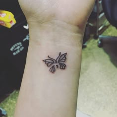 a small black and white butterfly tattoo on the left inner wrist, with an arrow in the middle