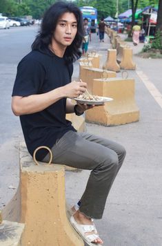 a man sitting on a bench holding a plate with food in his hand and looking at the camera