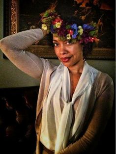 a woman with a flower crown on her head posing for a photo in front of a painting