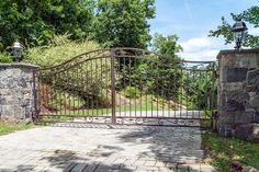 an iron gate in front of a stone wall and brick walkway leading to a grassy area