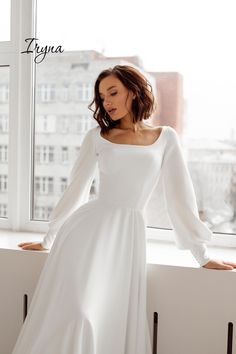 a woman in a white dress leaning against a window sill with her hands on her hips