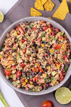 a bowl filled with mexican salad next to tortilla chips and lime wedges