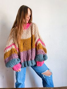 a woman standing in front of a wall wearing a sweater with multicolored stripes