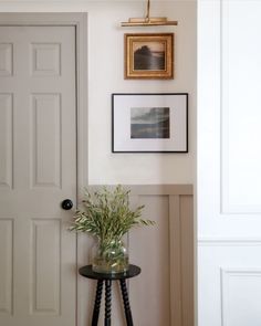 a small table with a plant on it in front of a door and framed pictures