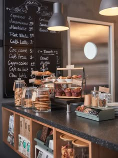 an assortment of pastries and desserts on display at a cafe counter in front of a chalkboard