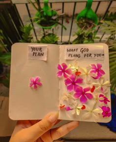 a person holding up a book with flowers on the pages and what god plans for you written on it