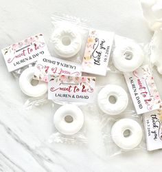 white donuts with labels on them sitting next to flowers and plastic wrappers for wedding favors