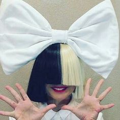 a woman with black hair wearing a white bow tie and holding her hands in front of her face