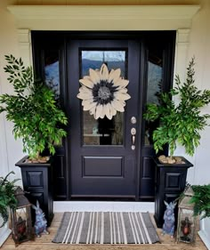 a black front door with two potted plants and a rug on the floor next to it