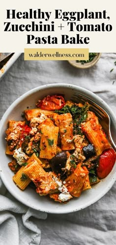 a white bowl filled with pasta and vegetables on top of a table next to a fork