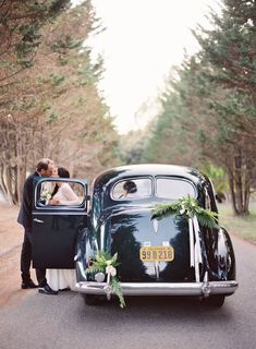 a bride and groom kissing in the back of an old car with greenery on it