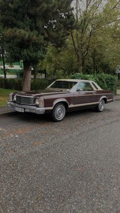 an old car is parked on the side of the road in front of a tree