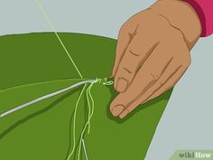 someone is cutting the end of a green piece of cloth with scissors and thread on it