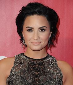 a close up of a person wearing earrings on a red carpet with a wall in the background