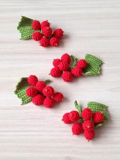 three crocheted cherries with leaves and berries on the top one is red