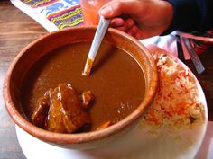 a person holding a spoon in a bowl filled with food on top of a plate