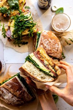 a person holding a sandwich in front of some other sandwiches on paper with condiments