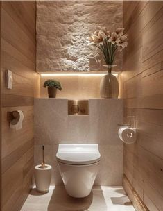 a white toilet sitting inside of a bathroom next to a vase with flowers on it