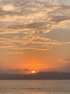 the sun is setting over the ocean with mountains in the background