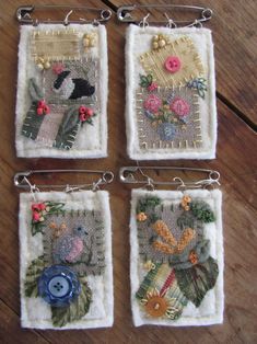 four small squares with flowers and birds in them on a wooden surface, hanging from metal hooks