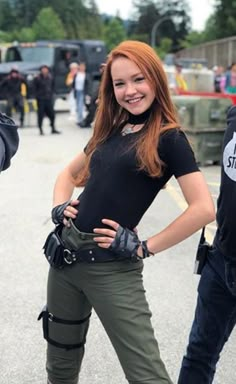 a woman in black shirt and green pants standing next to police