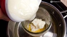 a person is pouring milk into a small bowl with corn and cheese in it on the stove