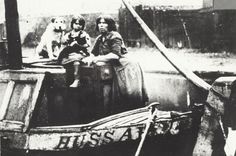 an old black and white photo of two people on a boat with a dog